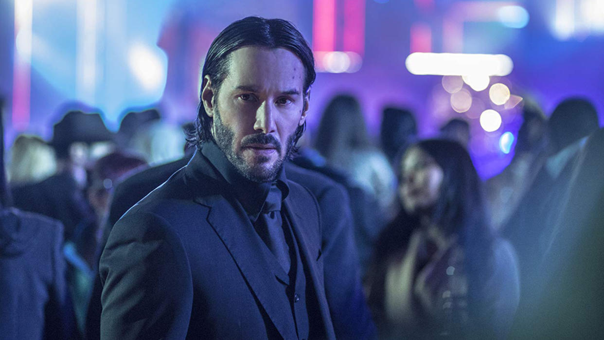  A rain soaked John Wick searches for someone in a neon setting in one of his movies. 