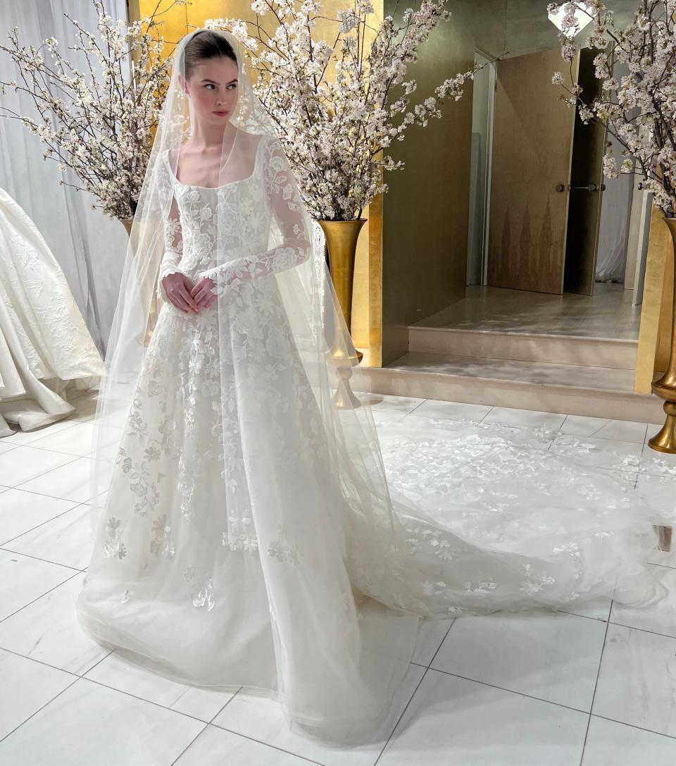 A woman stands in a floral wedding dress and veil.