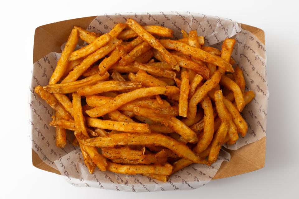 A close-up of a cardboard tray filled with seasoned french fries on patterned paper