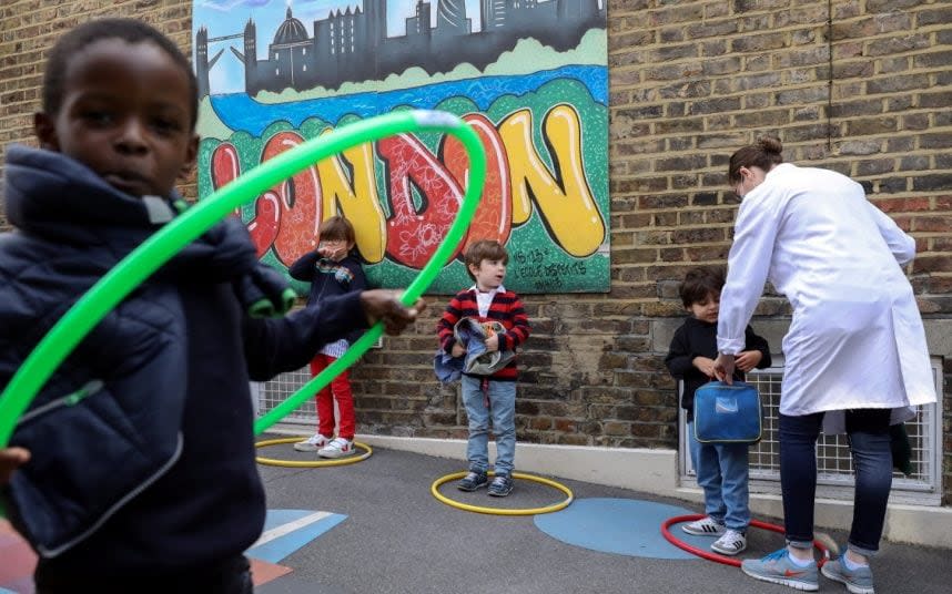 Children in the playground at L'Ecole des Petits, an independent French bilingual school in Fulham, learn how to stand in socially distanced hoops - KEVIN COOMBS/REUTERS