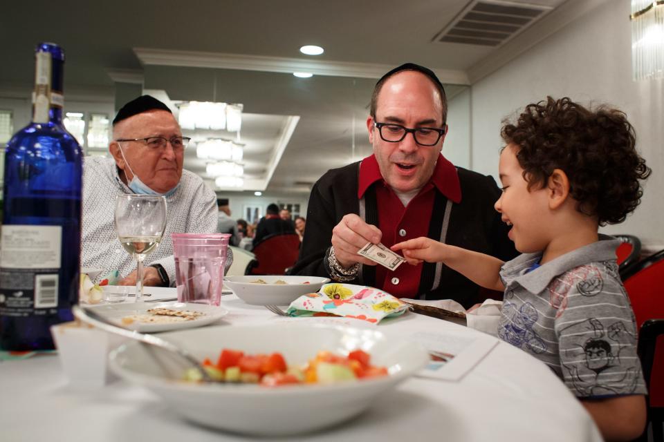 David Wolnerman watches as son Michael gives Tavi Waltman, 4, $5 for finding the afikomen, a piece of matzah that is traditionally hidden, after the family's Passover Seder in 2021.