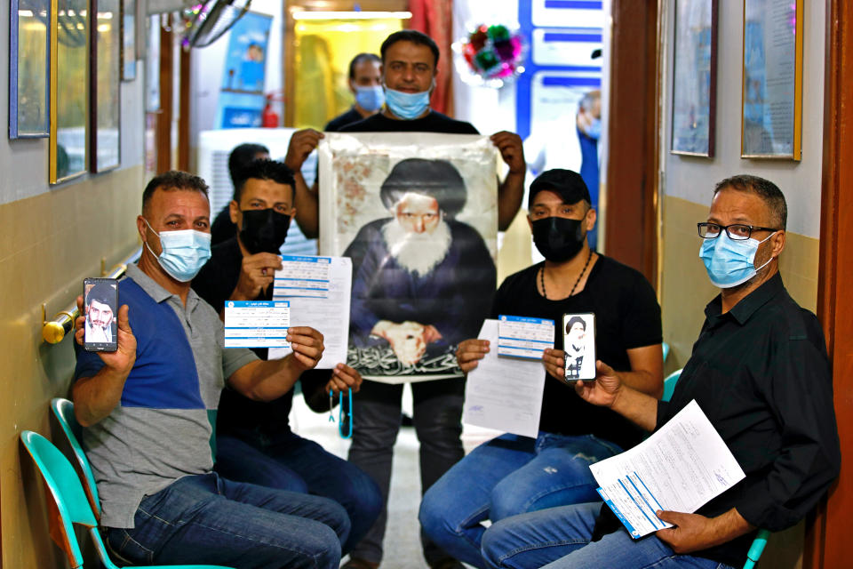 Followers of Shiite cleric Muqtada al-Sadr, pose for a photo holding pictures of him and his father and their vaccination cards as they wait to receive a Chinese Sinopharm vaccine at a clinic in Sadr City, Baghdad, Iraq, Wednesday, May 4, 2021. Iraq’s vaccine rollout had been faltering for weeks. Apathy, fear and rumors kept many from getting vaccinated despite a serious surge in coronavirus infections and calls by the government for people to register for shots. It took al-Sadr’s public endorsement of vaccinations — and images of him getting the shot — to turn things around. (AP Photo/Hadi Mizban)