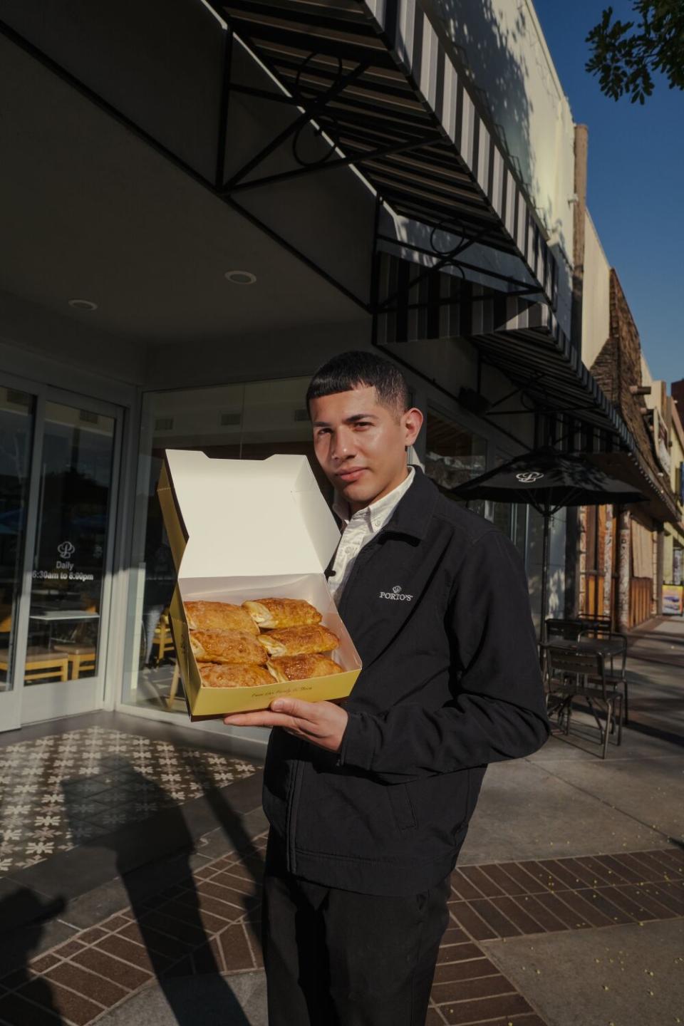 A man stands outside Porto's, holding open a to-go box of pastries.