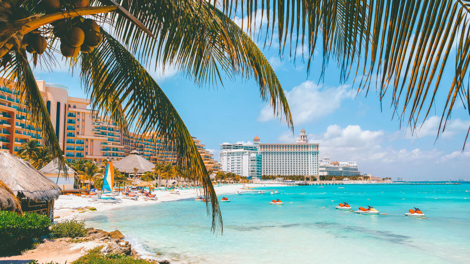 Cancun beach with hotels and plam tree in foreground.