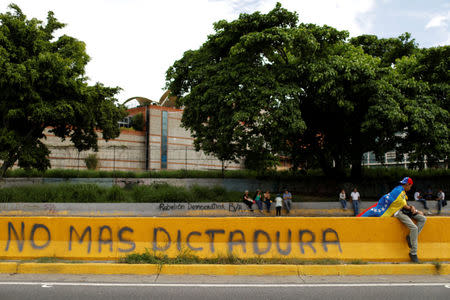 An opposition supporter with a Venezuelan national flag sits next to a graffiti that reads "No more dictatorship", during a protest against Venezuelan President Nicolas Maduro's government in Caracas, Venezuela May 15, 2017. REUTERS/Carlos Garcia Rawlins