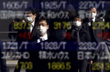 Pedestrians wearing masks are reflected in an electronic board showing various stock prices outside a brokerage in Tokyo, Japan