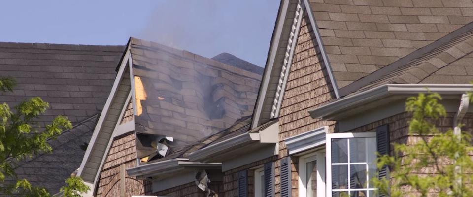 Fire damaged smoldering roof of a nondescript brick house.