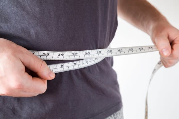 A man using a tape measure to measure his stomach.