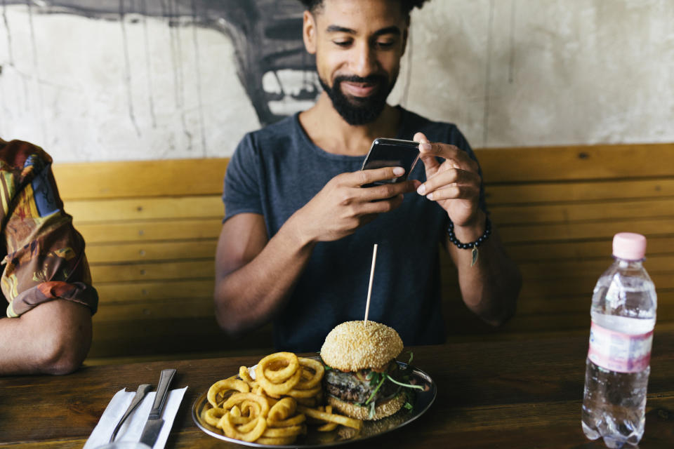 man taking a photo of his meal of curly fries and burget