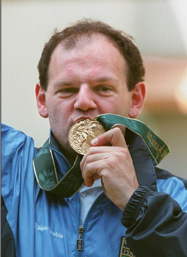 ATLANTA, GA - JULY 20:  Italy's Roberto Di Donna bites his gold medal after winning the men's air pistol competition at the Wolf Creek Shooting Complex 20 July in Atlanta. China's defending Olympic champion Wang Yifu, who took the silver, collapsed seconds after taking his final shot and was carried out of the area on a stretcher. (FOR EDITORIAL USE ONLY) AFP/IOPP-Michel GANGNE  (Photo credit should read MICHEL GANGNE/AFP via Getty Images) (Photo: MICHEL GANGNE via Getty Images)