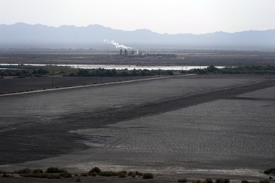 FILE - A dried up portion of the Salton Sea stretches out with a geothermal power plant in the distance in Niland, Calif., Thursday, July 15, 2021. Demand for electric vehicles has shifted investments into high gear to extract lithium from geothermal wastewater around the rapidly shrinking body of water. The ultralight metal is critical to rechargeable batteries. (AP Photo/Marcio Jose Sanchez, File)