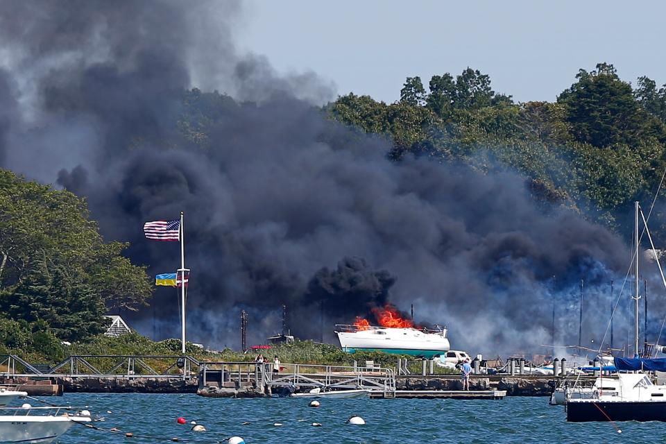 Crews battle a massive fire that has destroyed buildings, cars and vessels at a boat yard in Mattapoisett on Friday, Aug. 19, 2022.  The area of the fire was part of a Weather Service warning Friday of elevated fire risk due to drought and high winds. It sent a plume of dense black smoke over southeastern Massachusetts. (Peter Pereira/The Standard-Times via AP)