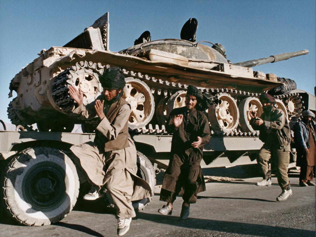 Three Taliban fighters stand in front of a tank.