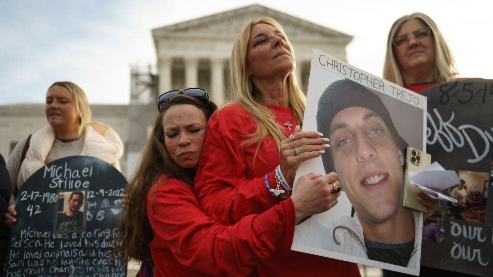 People holding signs and photos about family members who died