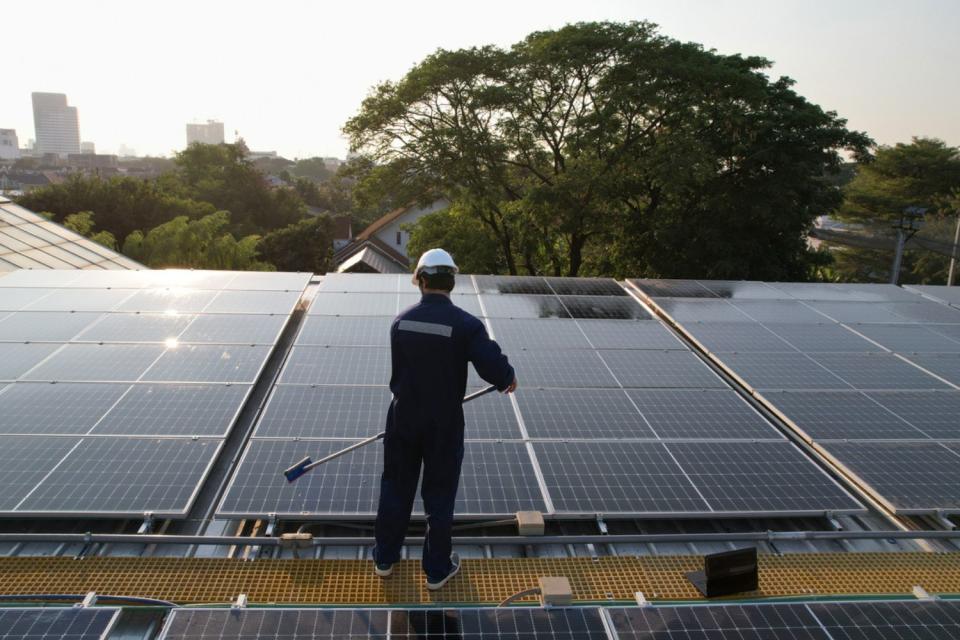 A worker in a blue work suit uses a tool to clean solar panels. 