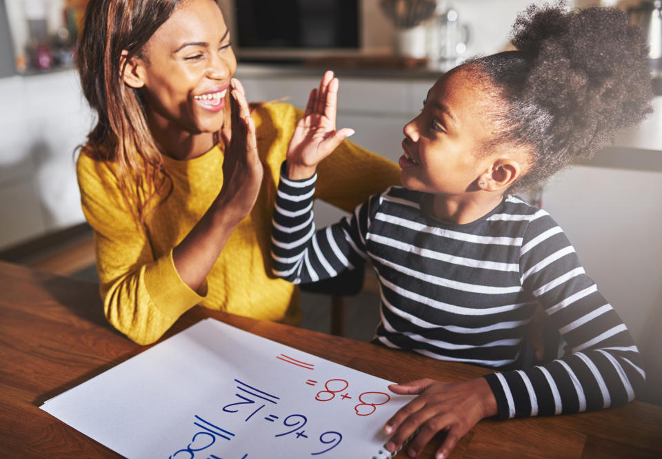 A woman and a child high-five while sitting at a table with math equations on a paper. The woman wears a yellow sweater; the child wears a black and white striped shirt