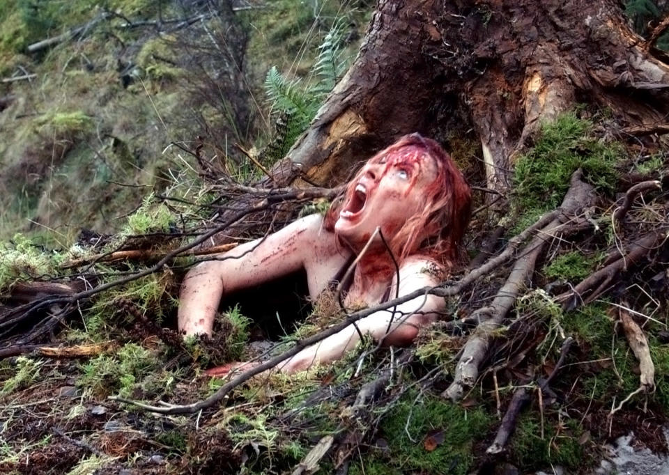 A woman covered in blood, screaming, and peeking out of the ground