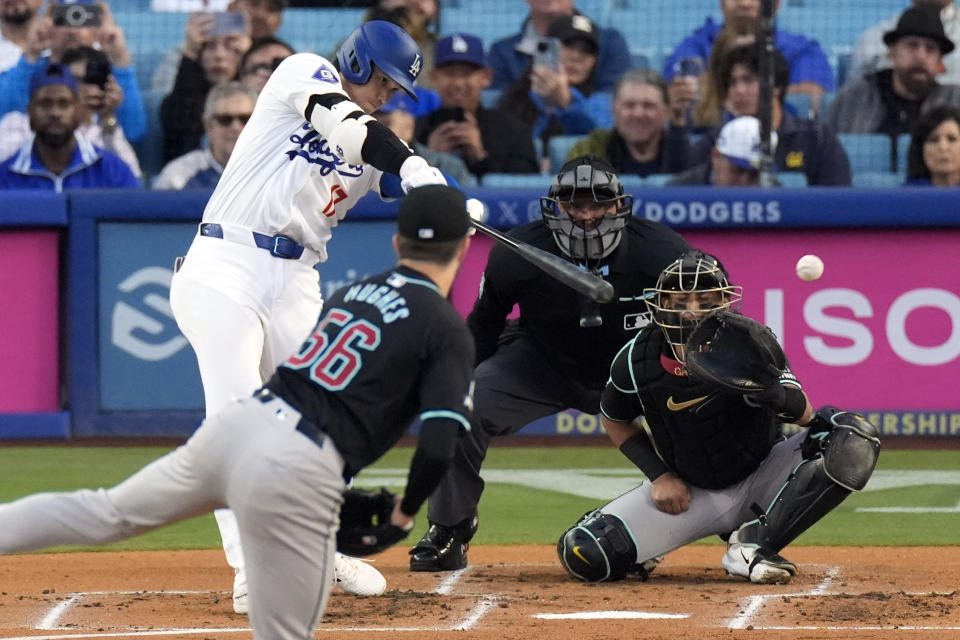 Los Angeles Dodgers' Shohei Ohtani, left, hits a single as Arizona Diamondbacks starting pitcher Brandon Hughes, second from left, and catcher Gabriel Moreno, right, watch along with home plate umpire Chad Fairchild during the first inning of a baseball game Wednesday, May 22, 2024, in Los Angeles. (AP Photo/Mark J. Terrill)