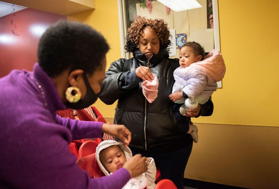 Starla Owens, center, picks up her 11-month-old daughter, Cherish, while Terita Carey, director of Childcare Wonderland in Columbus, Ohio, puts a coat on her nephew on Nov. 19, 2021.