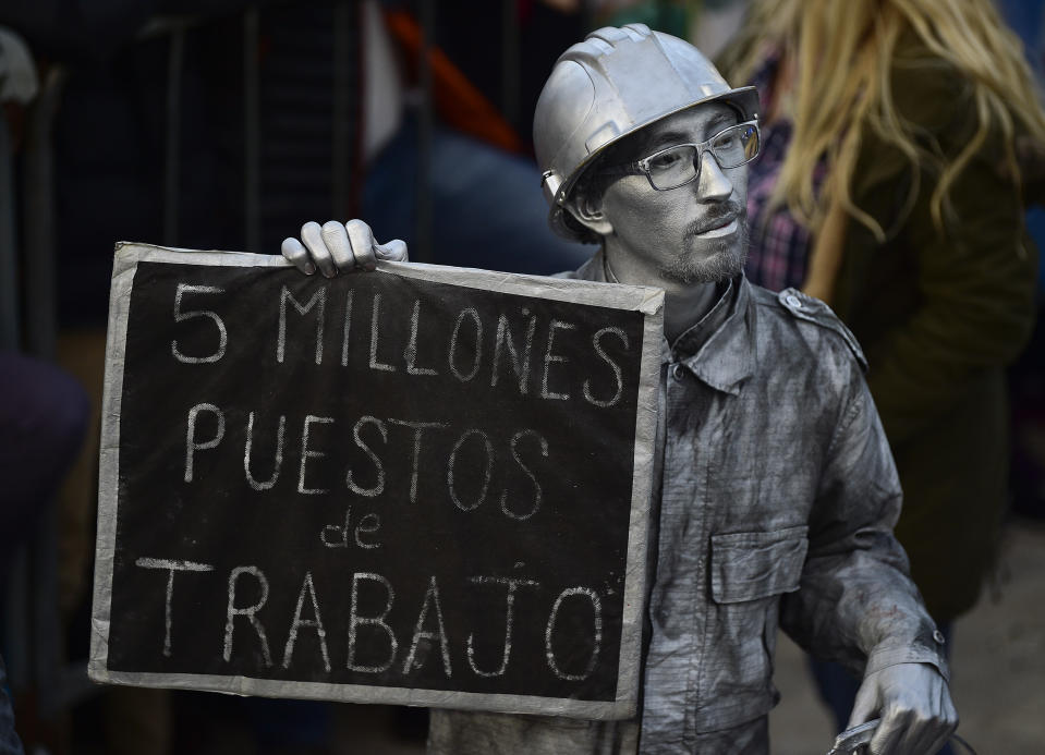 A man doused in silver body paint holds a sign with a message that reads in Spanish: "Five thousand jobs," in reference to the informal job market, attends the kick-off campaign rally of presidential candidate Alberto Fernandez and his running mate, former President Cristina Fernandez, in Buenos Aires, Argentina, Saturday, May 25, 2019. (AP Photo/Gustavo Garello)