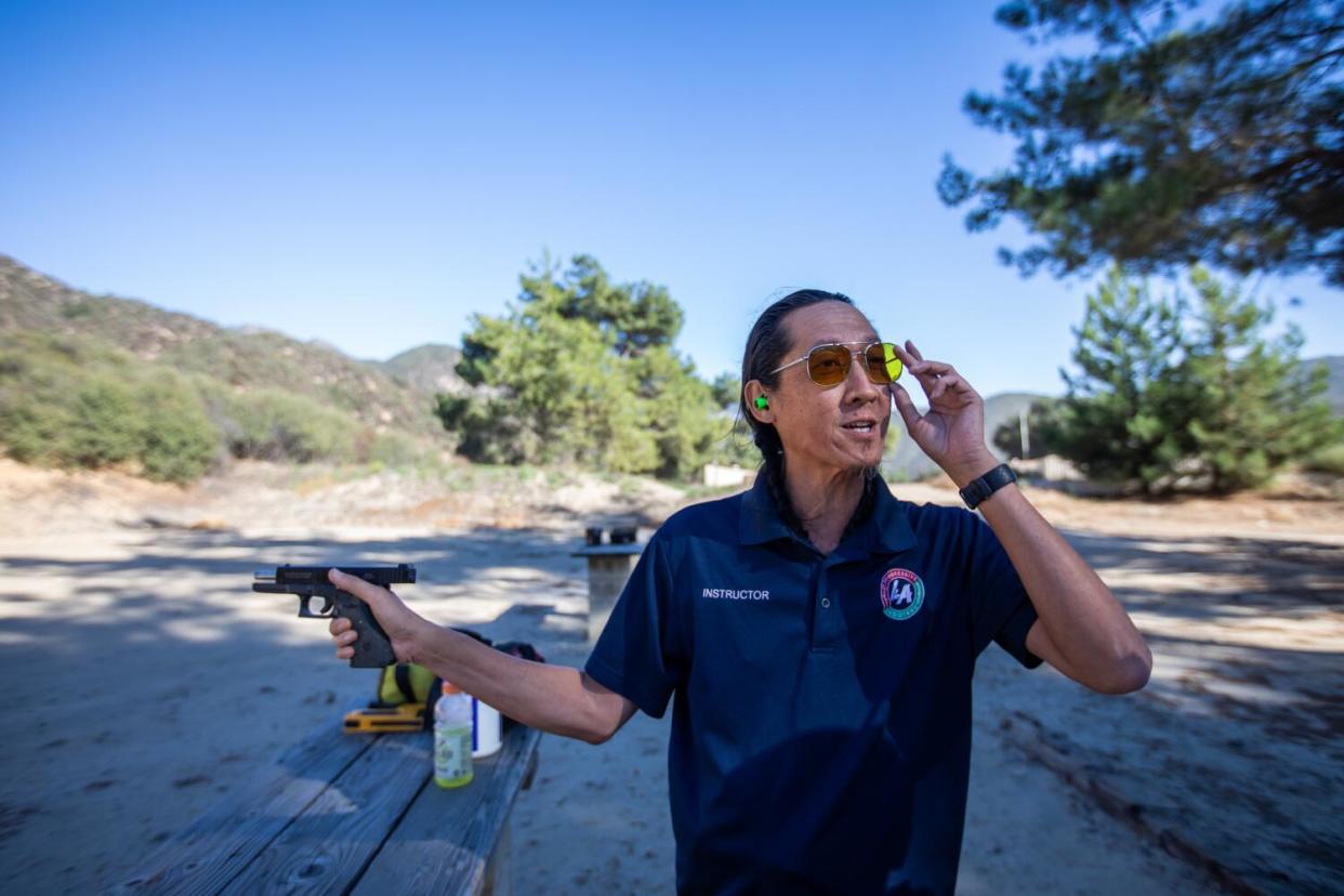 Tom Nguyen with a handgun and aviator sunglasses at a shooting range in a canyon