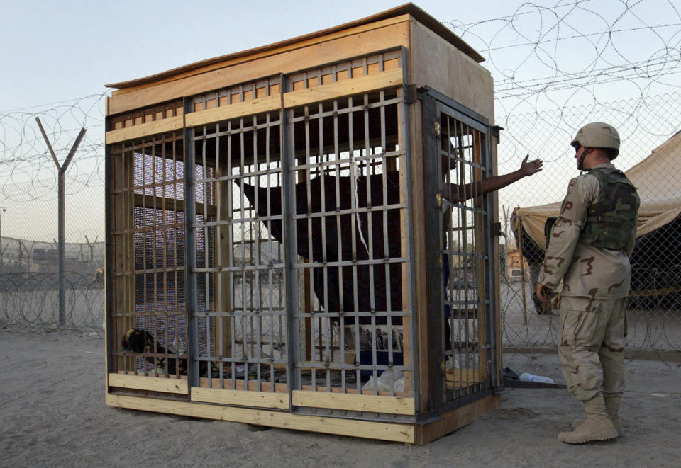 FILE - In this June 22, 2004, photo, a detainee in an outdoor solitary confinement cell talks with a military police officer at the Abu Ghraib prison on the outskirts of Baghdad, Iraq. A trial scheduled to begin Monday, April 15, 2024, in U.S. District Court in Alexandria, Va., will be the first time that survivors of Iraq’s Abu Ghraib prison will bring their claims of torture to a U.S. jury. Twenty years ago, photos of abused prisoners and smiling U.S. soldiers guarding them shocked the world. (AP Photo/John Moore, File)