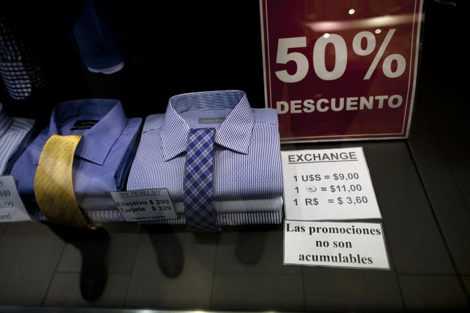 In this June 5, 2013 photo, a shop window displays a sign that reads in Spanish "50% discount" as well as the store's accepted rates of exchange in the informal market for the Argentine peso with the US dollar, the euro, and Brazil's real, along Florida street in Buenos Aires, Argentina. The weakening peso has led to a flood of day-trippers from neighboring countries into Argentina, which imposed severe currency controls in hopes of reducing the flight of dollars and protecting foreign reserves. (AP Photo/Natacha Pisarenko)