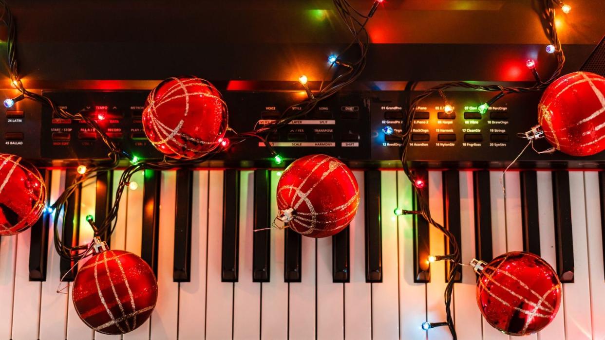piano keyboard with colorful christmas string lights, red ornaments, closeup
