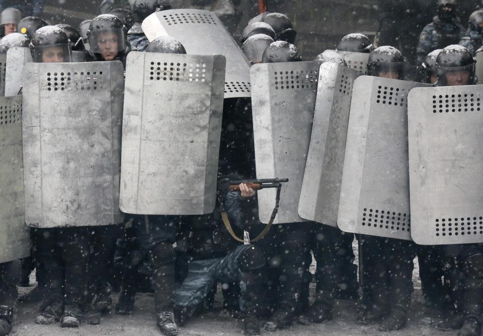 FILE - In this Wednesday, Jan. 22, 2014 file photo a police officer aims his shotgun during clashes with protesters in central Kiev, Ukraine. After two months of anti-government protests, modern Ukraine has never been so bitterly polarized. To be sure, Ukraine has long been divided. Russia and Europe have vied for dominance for centuries, causing deep cultural differences between the mostly Ukrainian-speaking western and central regions on the one hand, and the Russian-speaking east and south on the other. But as the crisis has deepened, each side has grown stronger in its convictions, and those who stood in the middle have been forced to choose sides. (AP Photo/Efrem Lukatsky, file)