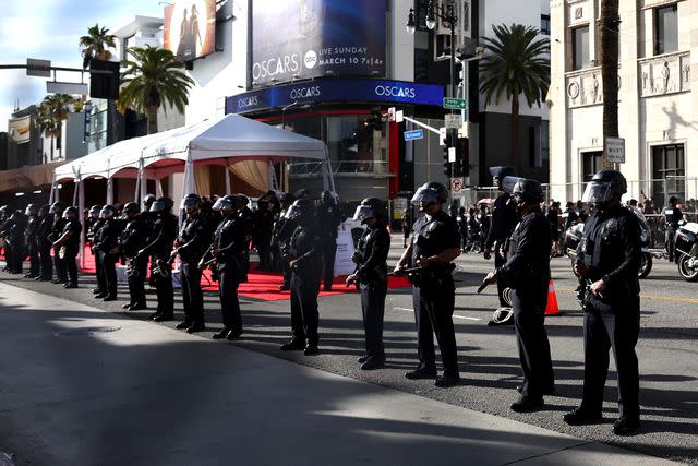 <p>Mario Tama/Getty</p> Police keep watch near protestors gathered outside the 96th Academy Awards