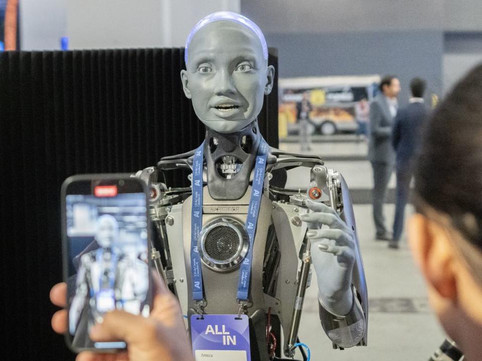  People take photos of an AI robot at the All In artificial intelligence conference in Montreal.