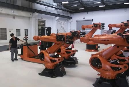 A staff member stands next to robots at a plant of Kuka Robotics in Shanghai in this August 13, 2014 file photo. REUTERS/Pete Sweeney