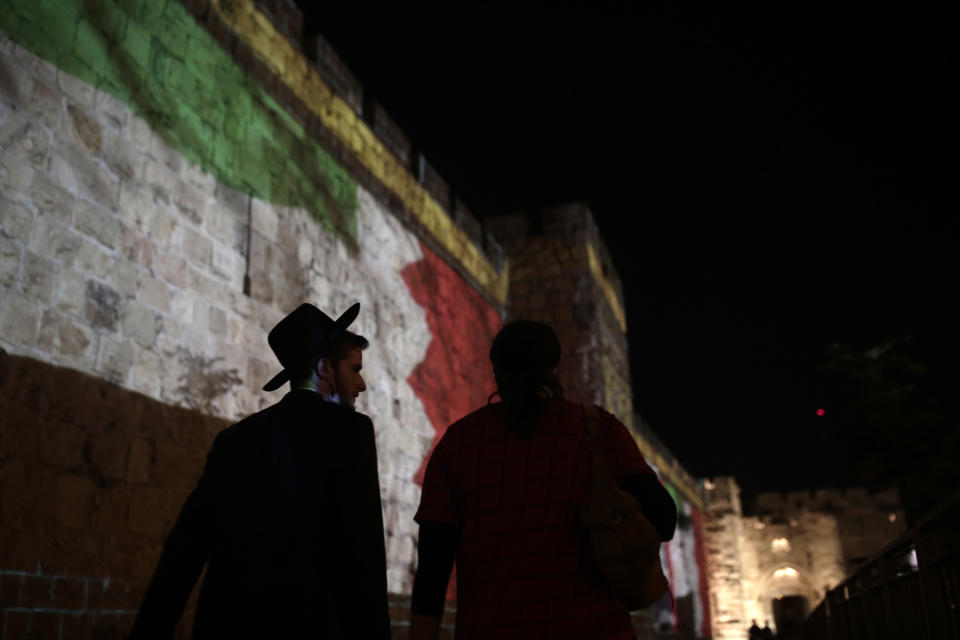 A couple walks past representations of the Emirati and Bahraini flags projected onto the walls of Jerusalem's Old City, marking the day of a signing ceremony in Washington signifying the two Gulf nations' normalization of relations with Israel, Tuesday, Sept. 15, 2020. (AP Photo/Maya Alleruzzo)