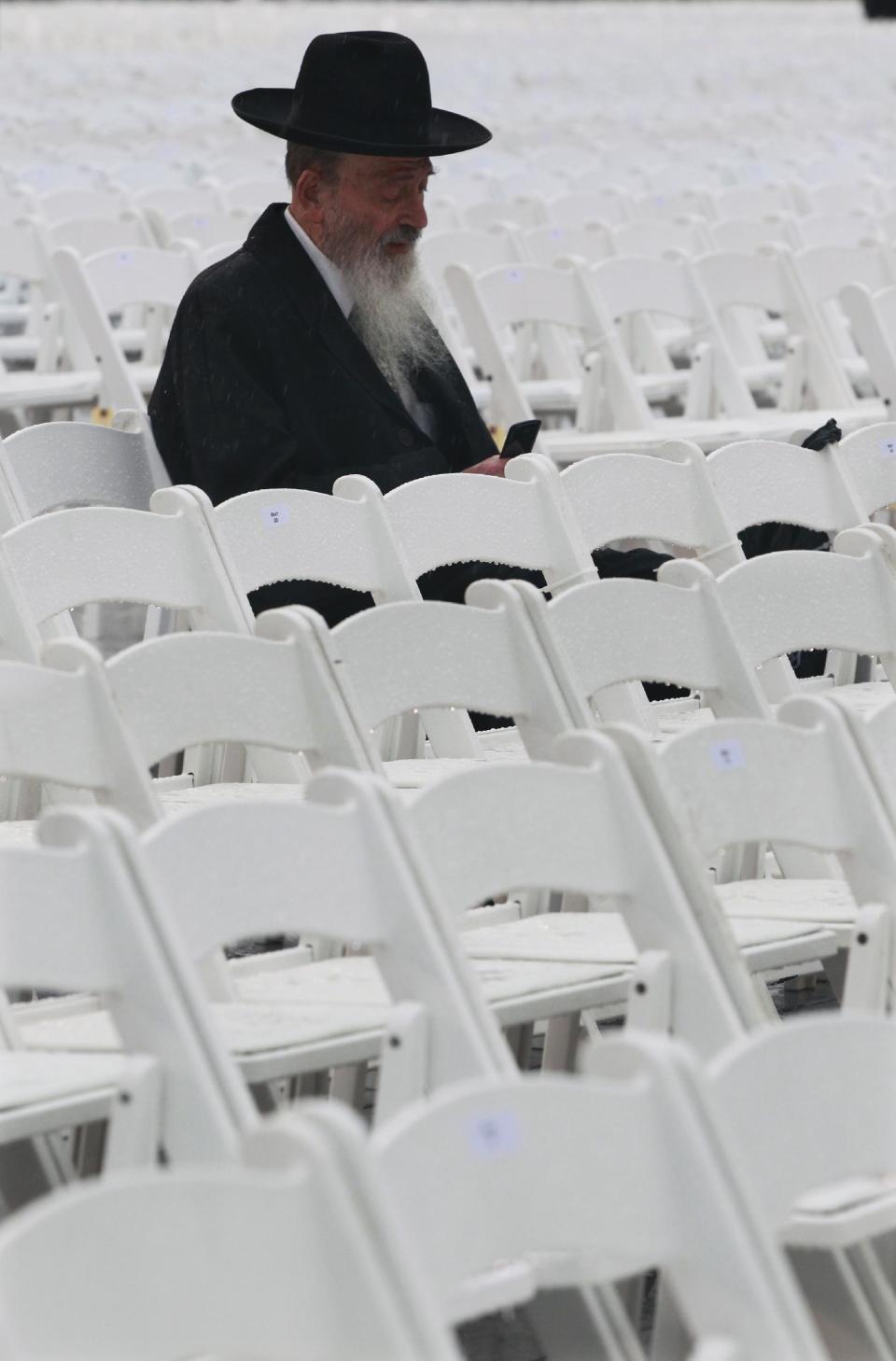 Joseph Luria sits in a light rain at MetLife stadium in East Rutherford, N.J, Wednesday, Aug. 1, 2012, as he waits for the start of the celebration Siyum HaShas. The Siyum HaShas, marks the completion of the Daf Yomi, or daily reading and study of one page of the 2,711 page book. The cycle takes about 7½ years to finish.This is the 12th put on my Agudath Israel of America, an Orthodox Jewish organization based in New York. Organizers say this year's will be, by far, the largest one yet. More than 90,000 tickets have been sold, and faithful will gather at about 100 locations worldwide to watch the celebration. (AP Photo/Mel Evans)