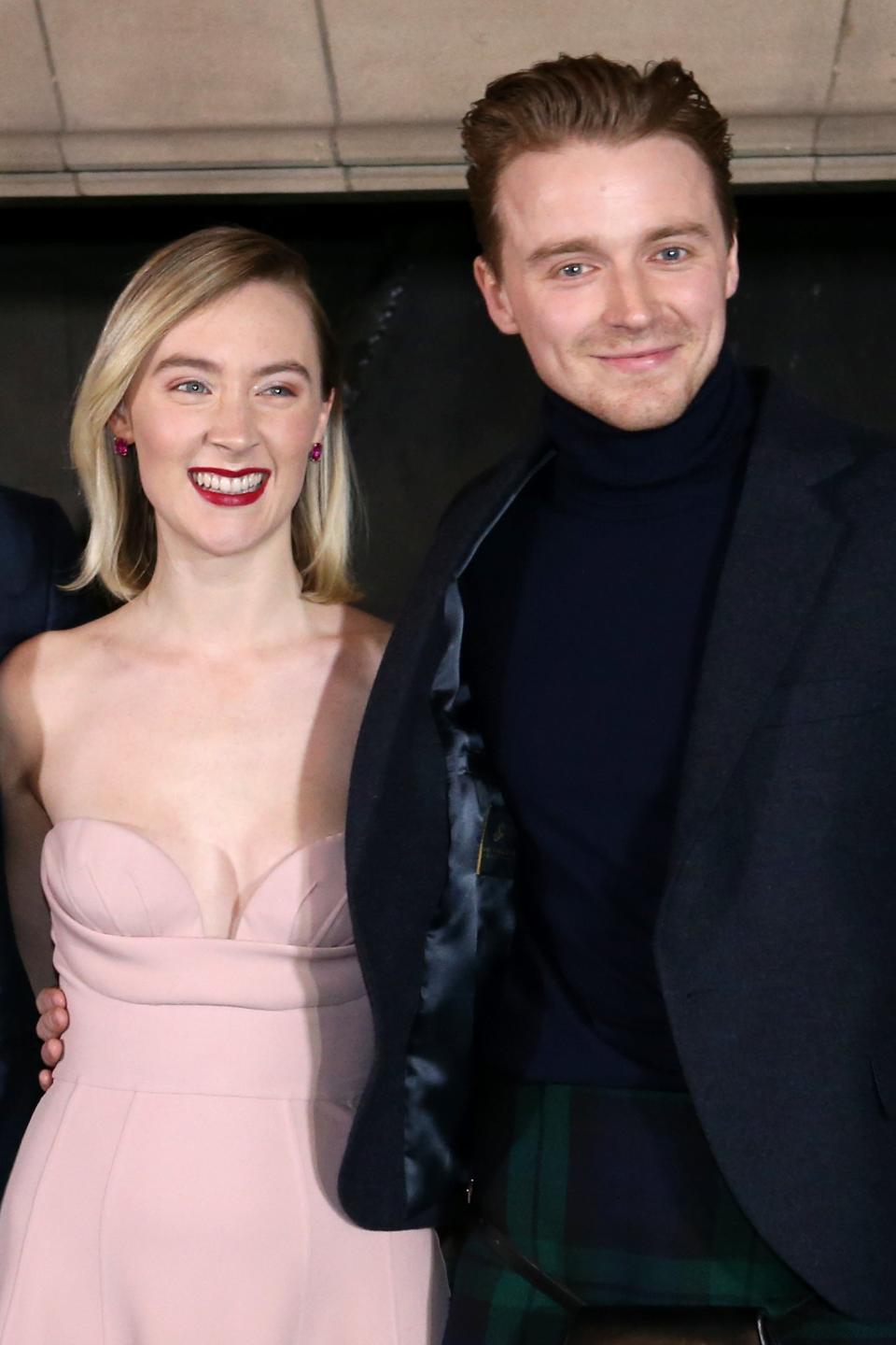 Joe Dempsie, Saoirse Ronan, and Jack Lowden pose together. Joe and Jack wear dark suits, while Saoirse wears a sleeveless dress with a sweetheart neckline