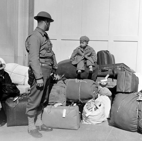 A boy sits on a pile of baggage as he waits for his parents, as a military policeman watches in San Francisco