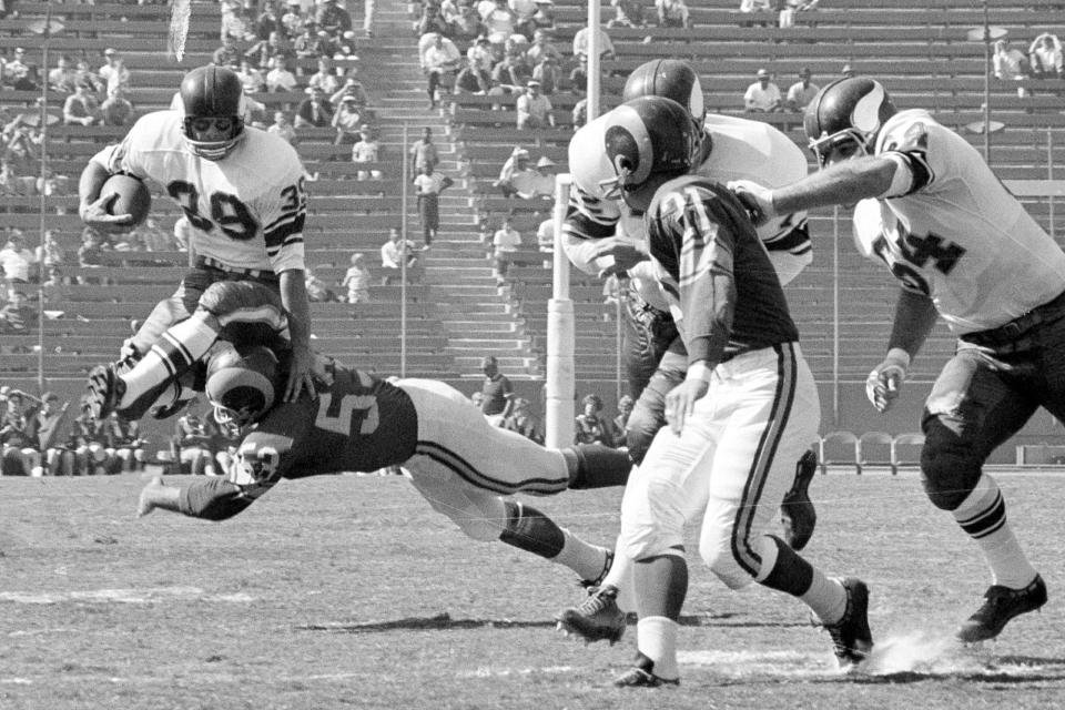 FILE - Minnesota Vikings halfback Hugh McElhenny, left, takes to the air to get past a Los Angeles Rams tackler during an NFL football game in  Los Angeles, on Oct. 21, 1962. McElhenny, an elusive NFL running back nicknamed "The King," died on June 17, 2022, at his home in Nevada, his son-in-law Chris Permann confirmed Thursday, June 23, 2022. He was 93. (AP Photo/Harold Filan, File)