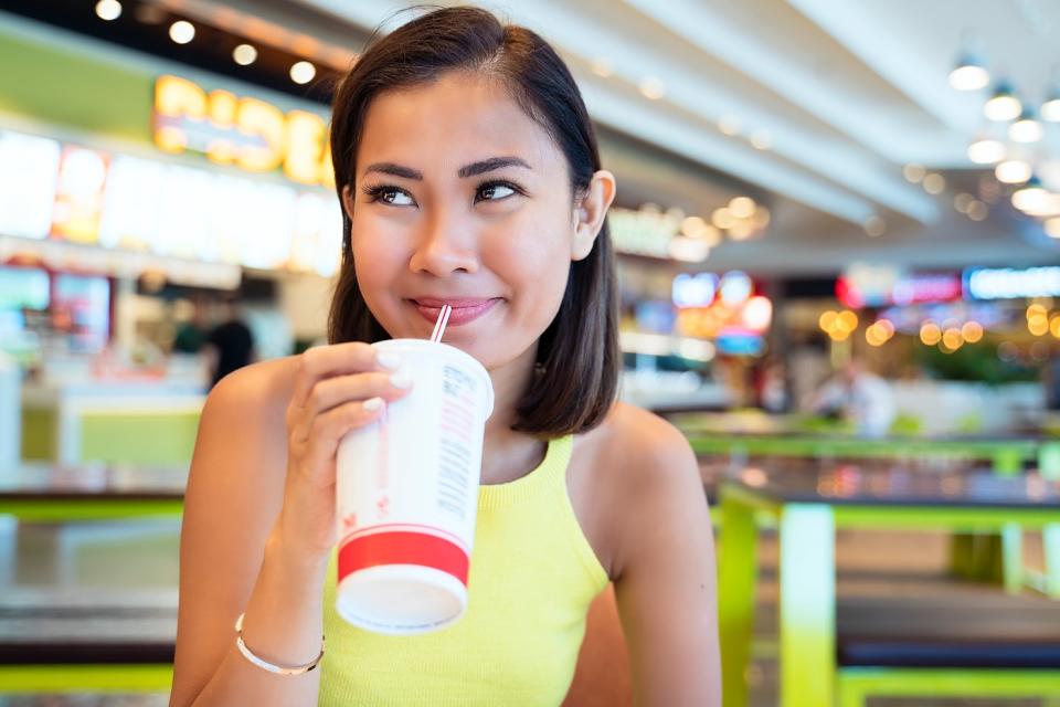 A person sips their drink through a straw while sitting in a food court.