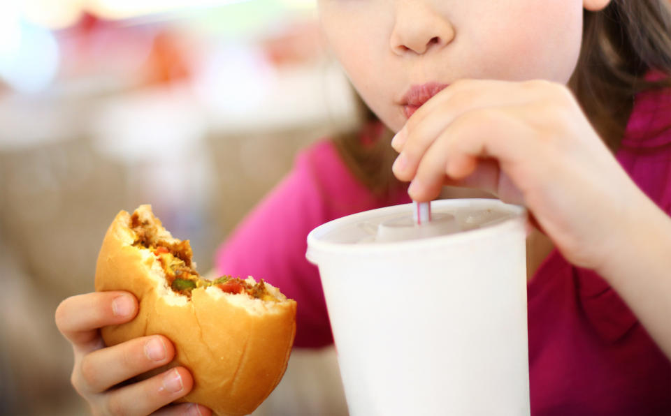 Closeup of little girl eating burger and drinking soda. Cut for unrecognition.The girl is elementary age and wearing pink t-shirt