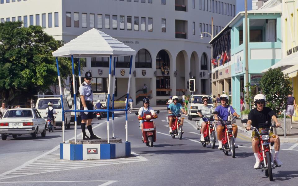 Tourists riding scooters past policeman in booth in Hamilton, Bermuda