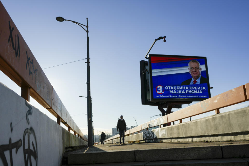 A man walks past a pre-election billboard showing convicted war criminal and Serbian Radical Party leader Vojislav Seselj, reading: "Homeland Serbia - Mother Rossia" in Belgrade, Serbia, Monday, Dec. 11, 2023. Serbia's President Aleksandar Vucic is pushing hard to reassert his populist party's dominance at this weekend's early parliamentary and local elections that observers say are being held in an atmosphere of intimidation and media bias. (AP Photo/Darko Vojinovic)