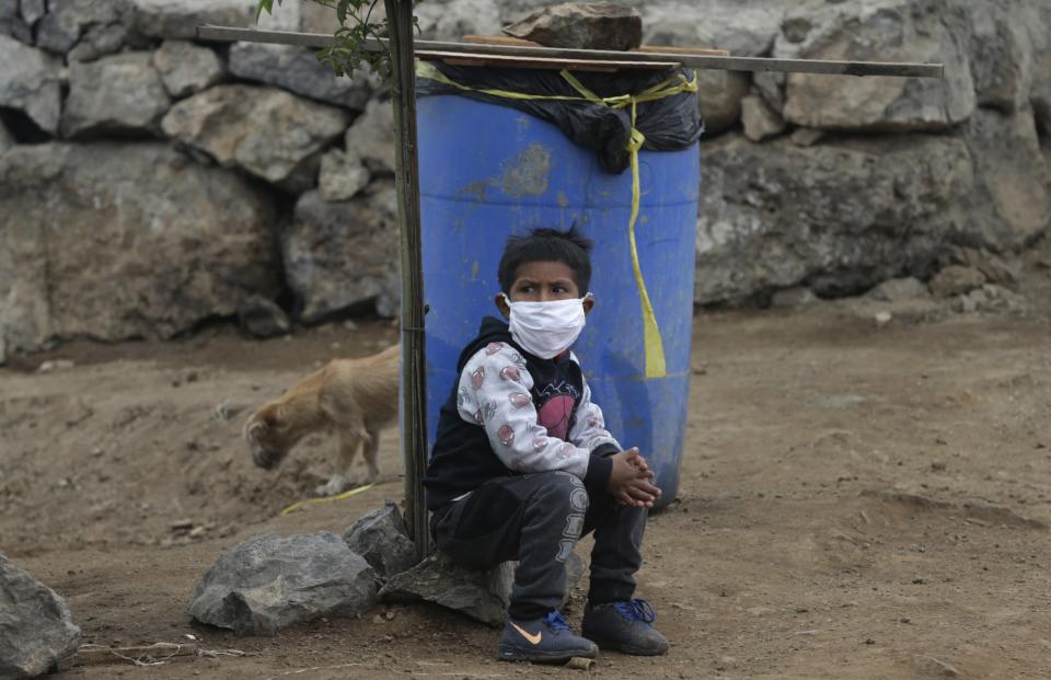 Wearing a protective face mask, a boy waits for his mother while she cooks for a group of families facing hardship due to the new coronavirus pandemic, in the Ticlio Chico shantytown of Lima, Peru, Monday, May 25, 2020. Families who have run out of money and have no present prospect of finding work during quarantine, are increasingly dependent on small community soup kitchens where those more fortunate donate food and a collective meal is served to the needy. (AP Photo/Martin Mejia)