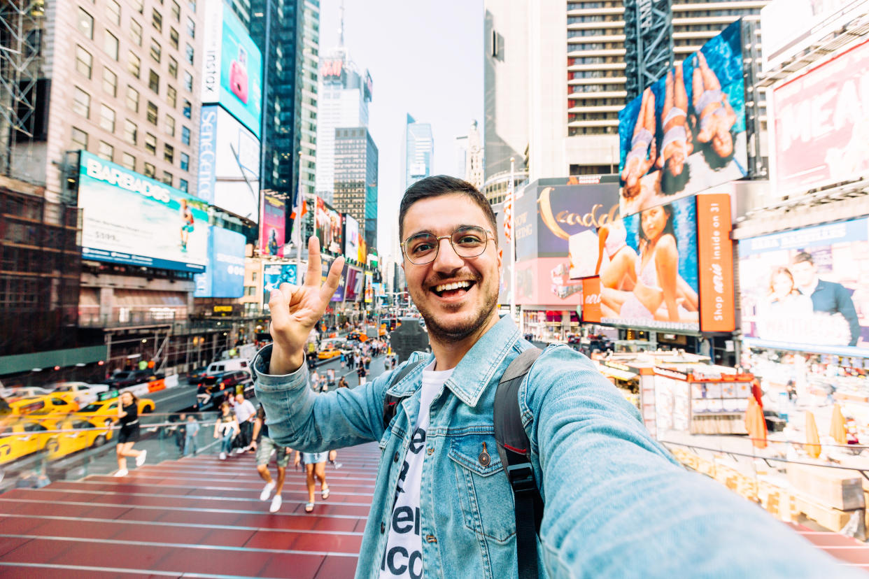 Young happy man taking selfie and showing peace gesture at Times Square, New York City, USA