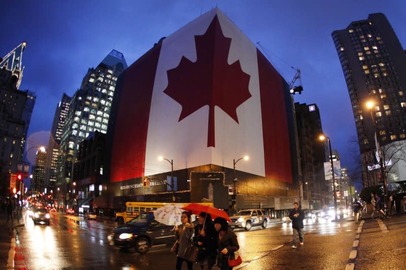 Pedestrians cross a street in front of a building under construction draped in a giant Canadian flag in downtown Vancouver on February 10, 2010. On January 28, 1965, British Queen Elizabeth II accepted a new national flag design for Canada that included a red maple leaf in its center. File Photo by Brian Kersey/UPI