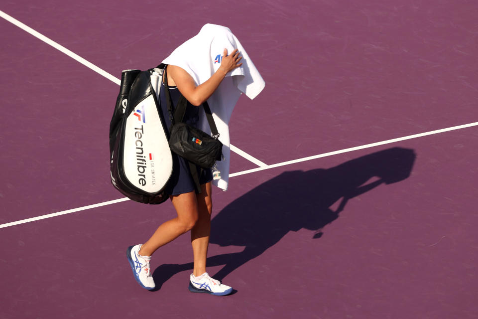 Iga Swiatek leaves the court with a towel covering her head.