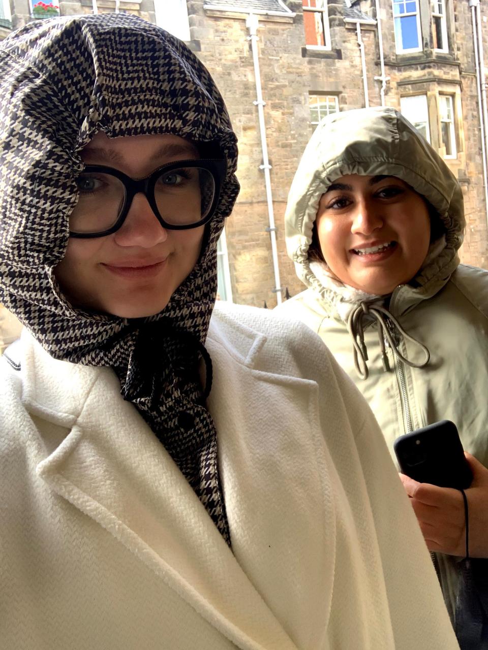 Two women with their jacket hoodies up, smiling.