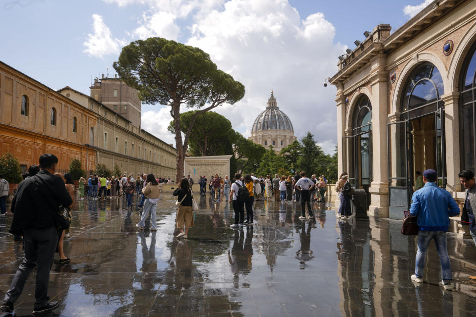 Visitors walk on a terrace of Vatican Museums, backdropped by St.Peter's Basilica, in Vatican City, Thursday, May 11, 2023. Work will continue until December to reveal the 4-meter- (13-foot-) tall Hercules, believed to have stood in ancient Rome’s Pompey Theater, to its original golden sheen. The discovery of the gilded bronze in 1864 during work on a banker’s villa near Piazza dei Fiori made global headlines. (AP Photo/Andrew Medichini)