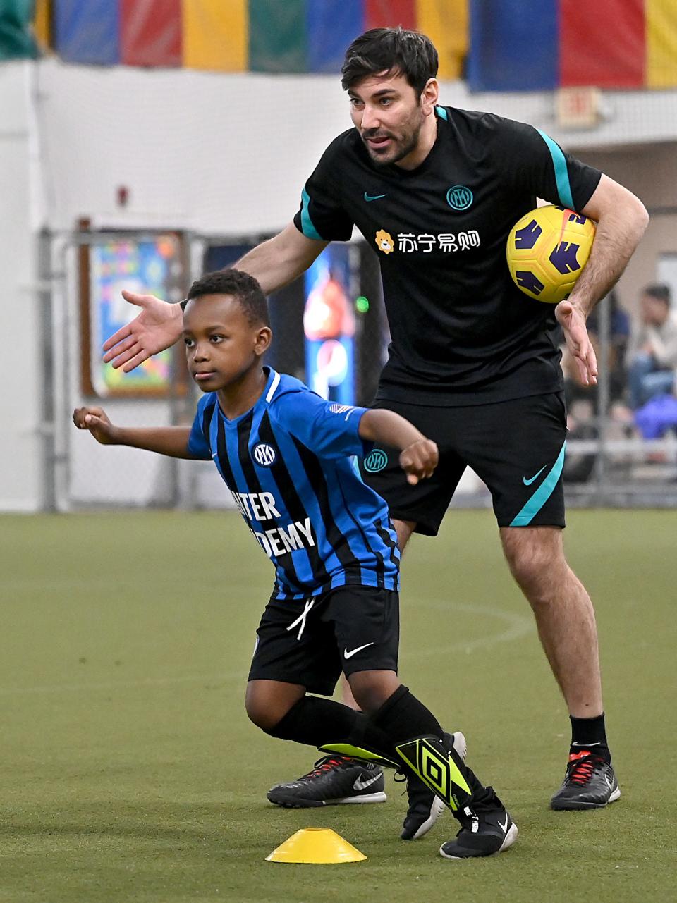 Christian Saintima, 6, of Framingham, learns soccer under the watchful eye of Luigi Mainolfi, a coach from an elite youth soccer academy in Milan, Italy, during an Inter Academy Metro West Boston practice at SMOC's Community and Cultural Center in Framingham, April 6, 2022. Mainolfi will be in Framingham for two weeks to train local Academy MetroWest Boston coaches and work with youth soccer players in MetroWest.