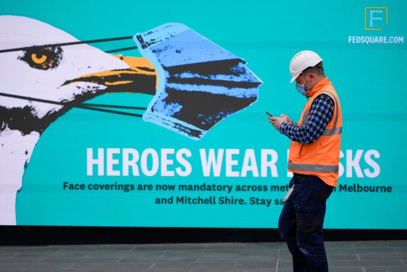 FILE PHOTO: An essential worker wearing a face mask walks past a 'Heroes Wear Masks' sign in Melbourne, the first city in Australia to enforce mask-wearing to curb a resurgence of COVID-19