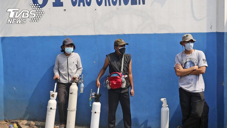 圖／達志影像美聯社，三位男子拖著氧氣瓶在補充站前等待。